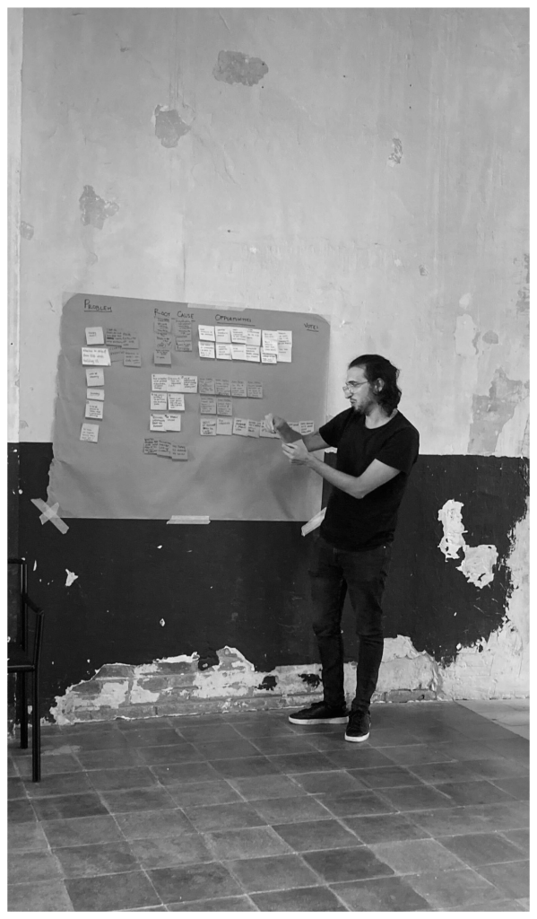 It  shows me standing and leading a workshop. I am pointing at a large board covered in sticky notes.