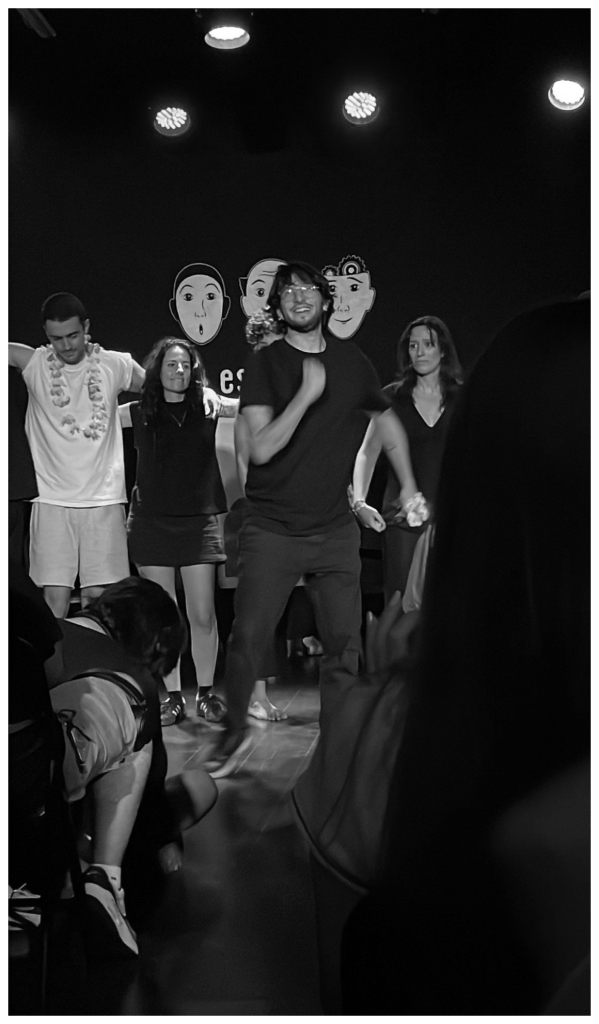 I am on a stage with a group of people, under bright stage lights. I am in the center, dancing energetically and smiling, seemingly as part of a performance or a fun group activity.